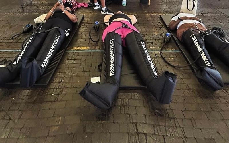Three guests relaxing in NormaTec compression boots at a Recovery1 pop-up