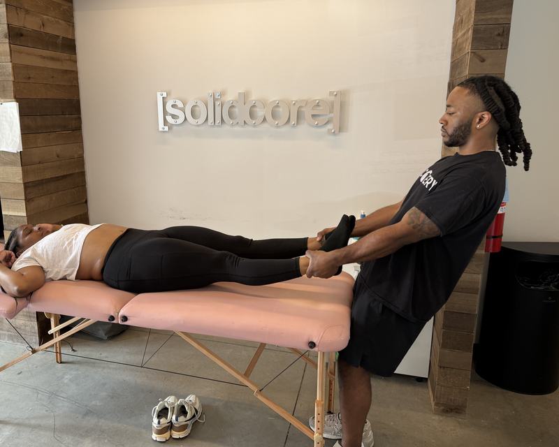 Elijah Small giving a client an assisted leg stretch on a massage table at a fitness studio